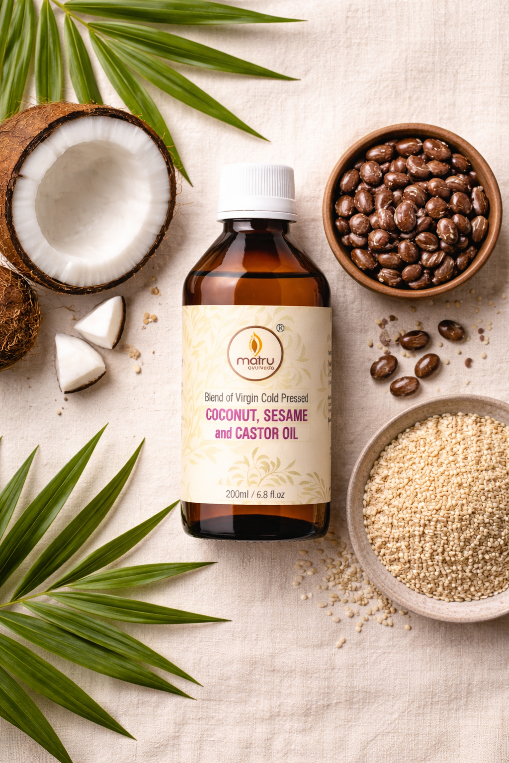 Raw ingredients of Matru Ayurveda hair oil blend — fresh coconut halves, castor seeds and sesame seeds with the bottle on a natural surface