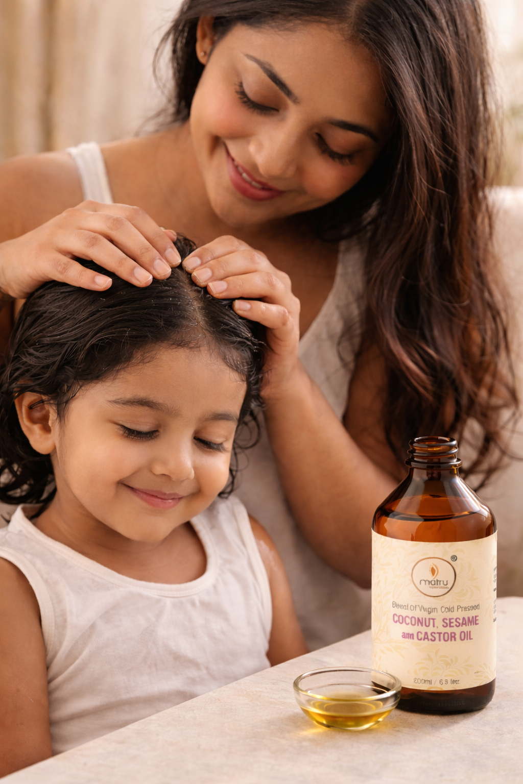 Mother applying natural ayurvedic hair oil to young child's hair — safe chemical-free coconut castor sesame blend for kids